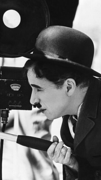 Charlie Chaplin is adjusting an old movie camera in this black and white portrait
