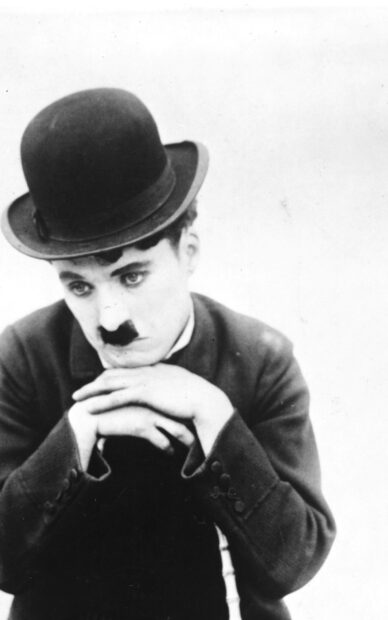 Charlie Chaplin wearing a bowler hat with hands folded looking thoughtful in a classic pose