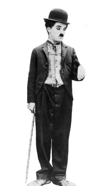 Charlie Chaplin dressed in his iconic costume holding a cane and looking down in black and white
