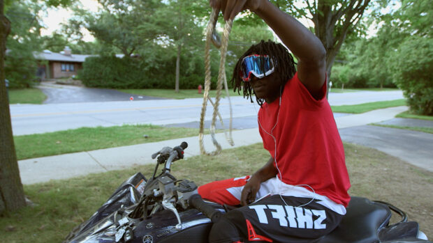 Chief Keef sitting on a bike wearing a red shirt and holding a chain outdoors