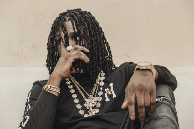 Chief Keef wearing multiple gold chains and jewelry while posing with hand near face