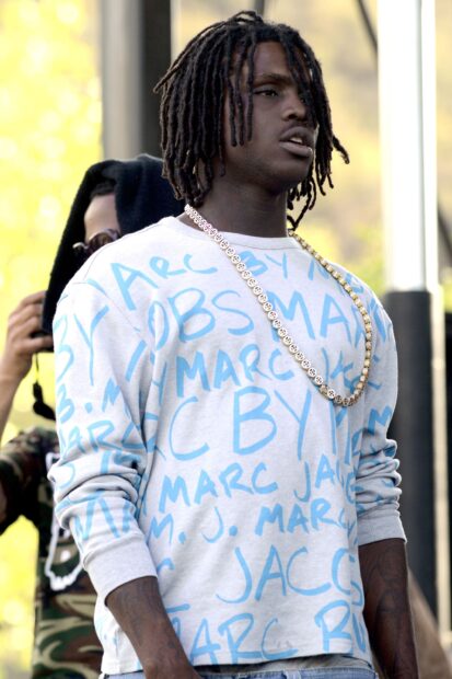 Chief Keef wearing a white and blue sweatshirt with dreadlocks standing outdoors