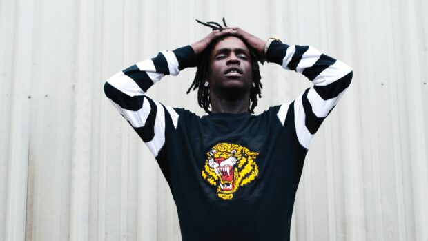 Chief Keef standing with hands on head wearing a black shirt with a tiger design