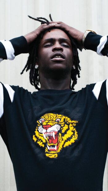 Chief Keef wearing a black sweatshirt with a roaring tiger design and hands on his head