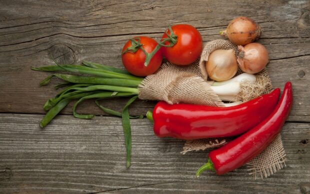 Fresh chili pepper and vegetables including tomatoes and onions on wooden surface