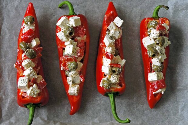 Red chili pepper filled with cheese cubes olives and herbs on a gray surface