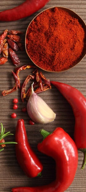 Fresh chili pepper and ground chili pepper with garlic on a wooden surface