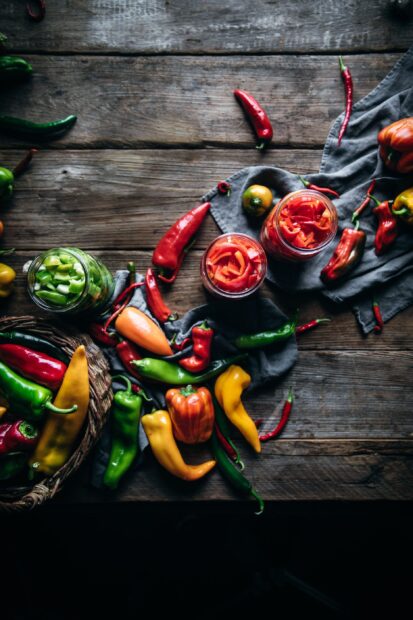 A variety of chili pepper placed on a wooden table with jars of sliced chili pepper