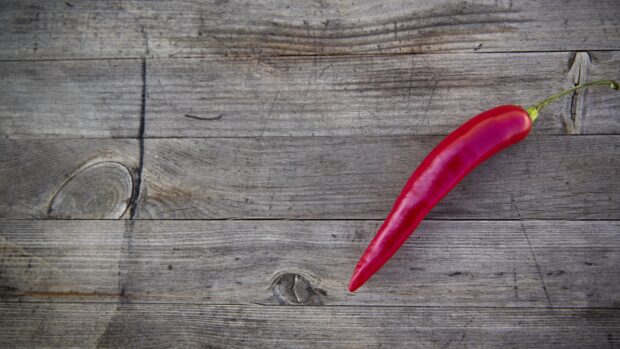 A single red chili pepper placed on a textured wooden surface