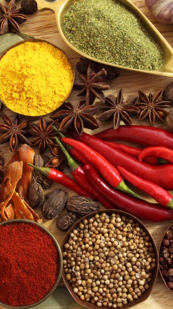 Fresh chili pepper surrounded by various spices on wooden surface