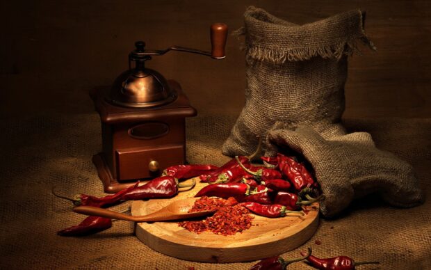 Red chili pepper with crushed chili on wooden board and vintage grinder on burlap surface