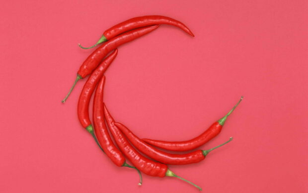 Fresh chili pepper arranged on a vibrant red surface forming a crescent shape