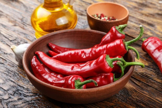 Fresh chili pepper placed in a wooden bowl on a rustic table with garlic and spices visible