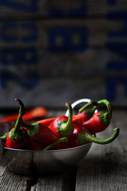Fresh chili pepper in a metal bowl on a rustic wooden surface