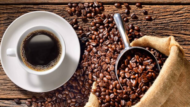 Fresh coffee beans spilling from a bag next to a cup of black coffee on a wooden table