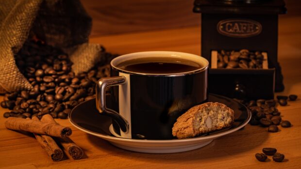 A cup of coffee with a cookie and coffee beans surrounding it on wooden table