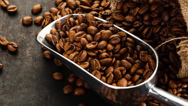 Close up of coffee beans in a metal scoop on a dark surface