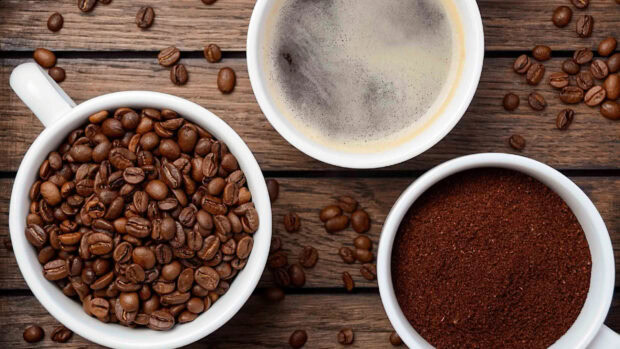 A close up of coffee beans ground coffee and a cup of brewed coffee on wooden table