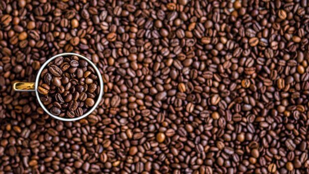 Close up view of coffee beans filling a cup and scattered around the surface