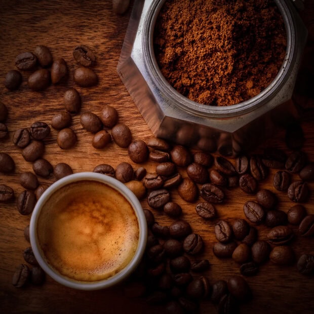 Coffee beans next to a cup of espresso and ground coffee on a wooden surface