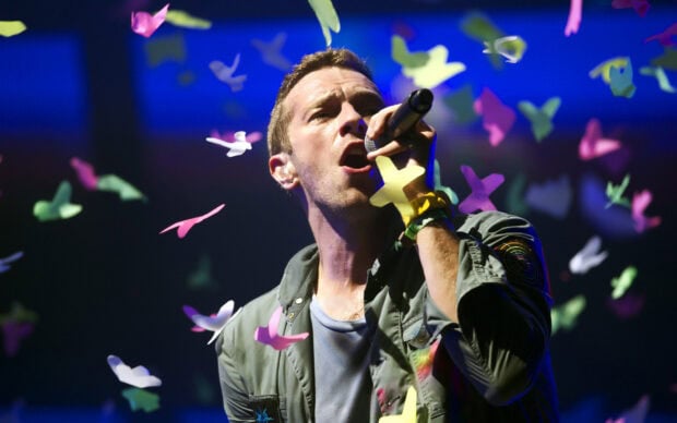 Coldplay singer performing live with colorful butterfly shapes around him on stage