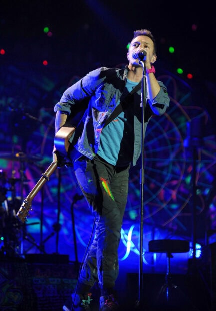 Coldplay singer performing live on stage with guitar during a concert