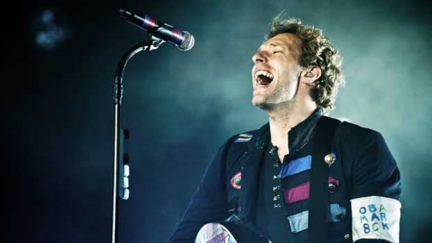 Coldplay performing passionately on stage during a live concert with a vintage military jacket