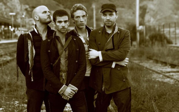Vintage style image of Coldplay band members standing outdoors near train tracks