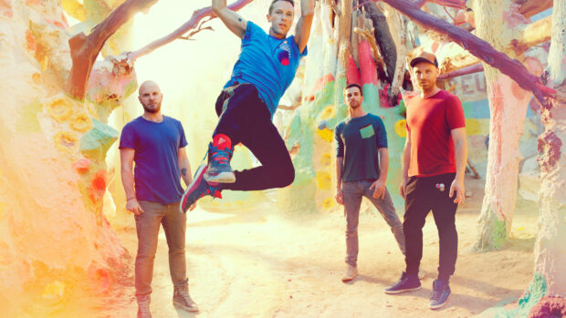 Coldplay band members posing in colorful outdoor setting with one jumping in the air