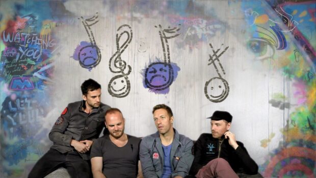 Coldplay band members sitting against a wall with musical notes graffiti artwork