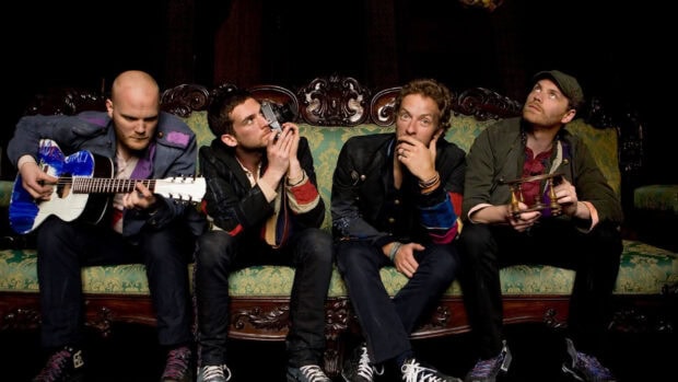 Coldplay band members sitting on an antique sofa with musical instruments in a vintage setting