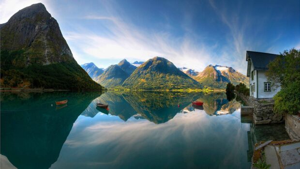 Mountain landscape with lake and small boats reflecting clouds and sky