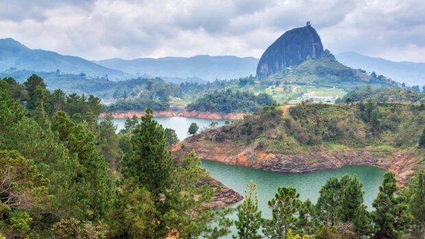 A scenic view of the Colombia landscape with lush greenery and a large rock formation in the distance