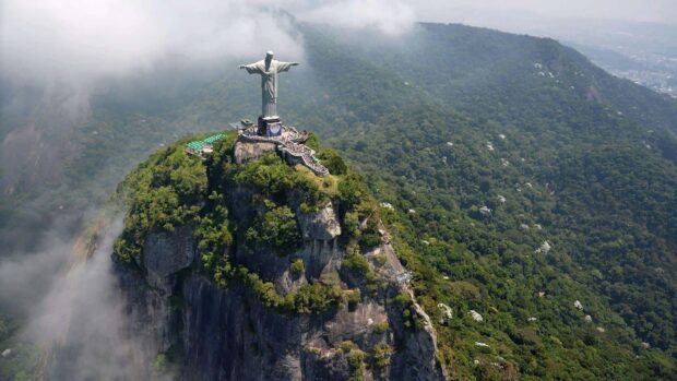 Aerial view of Corcovado Mountain with a statue overlooking dense forest and mist
