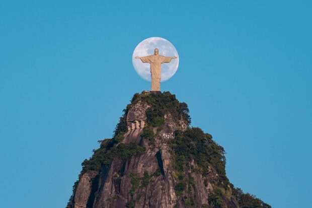 Christ the Redeemer stands on Corcovado Mountain during a full moon in clear blue sky