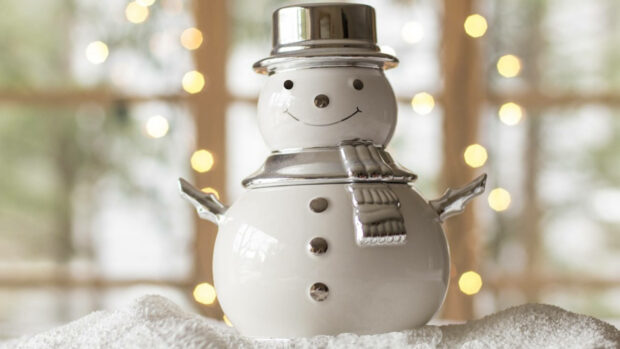 Ceramic snowman with silver hat and scarf on snowy surface with warm lights