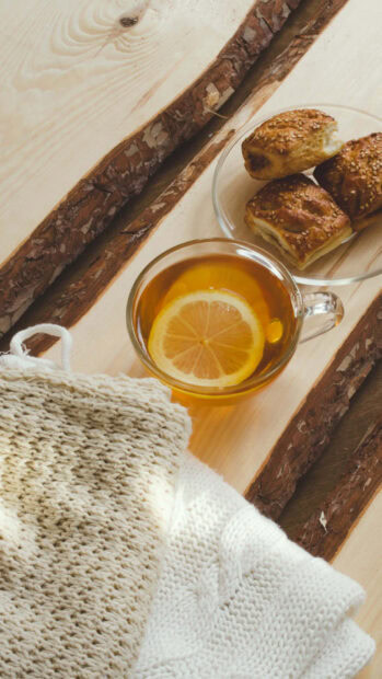 A warm knitted scarf with tea and fresh baked goods on a wooden table