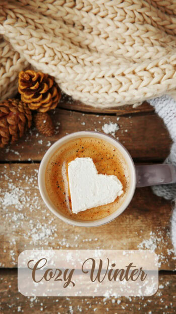 Heart shaped marshmallow in cozy winter setting with pinecones and knitwear on wooden table