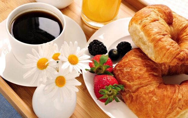 Fresh croissant with strawberries and blackberries on a plate next to a cup of coffee and a vase of daisies
