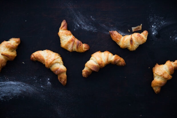 Freshly baked croissant spread on a dark surface with scattered flour dusting
