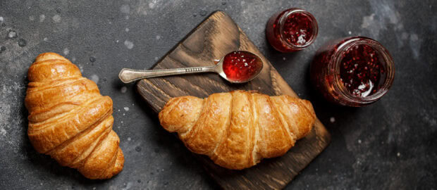 Fresh croissant placed next to jars of jam on a wooden board