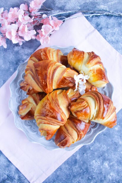 A plate of freshly baked croissant with golden brown crust placed on a pink cloth with flowers