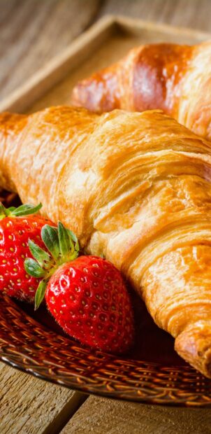 Fresh croissant with strawberries on a wooden plate placed on a rustic table