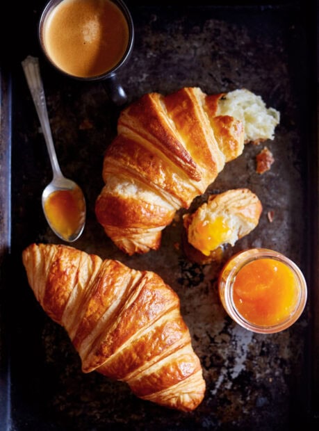 A close up of croissant with jam and coffee showing the flaky texture of croissant on a black tray