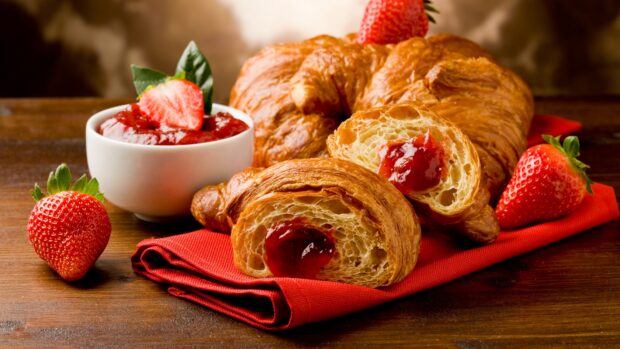 Fresh croissant with strawberry jam served on red cloth and wooden table