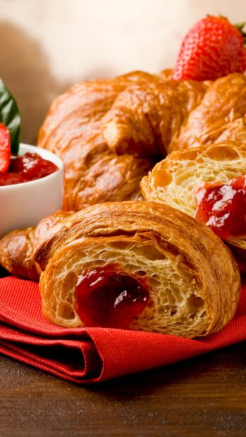 Fresh croissant with strawberry jam on a red napkin and fresh strawberries nearby