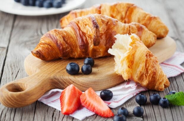 A fresh croissant with flaky layers served with strawberries and blueberries on a wooden board