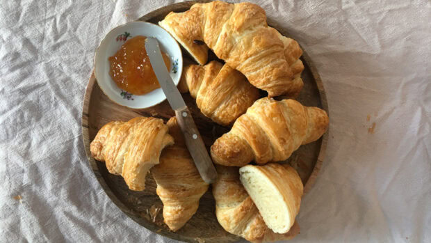 Fresh croissant with jam and a knife on a wooden plate