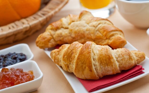 A close up of croissant placed on a white plate with jam in the background