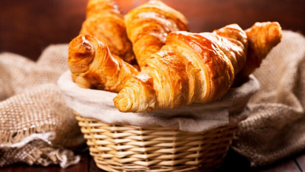 Fresh golden croissant placed in a woven basket with a cloth lining
